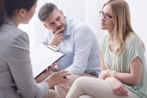 Upset young woman talking to a female psychologist, with her husband aside