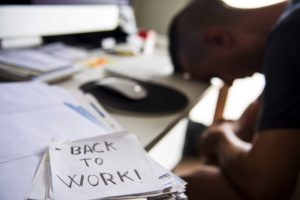 closeup of a concerned man sitting at his office desk and a note in the foreground with the text back to work handwritten in it