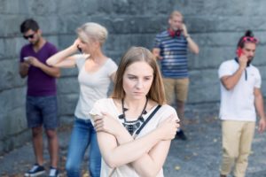 Sad girl standing among people using their phones