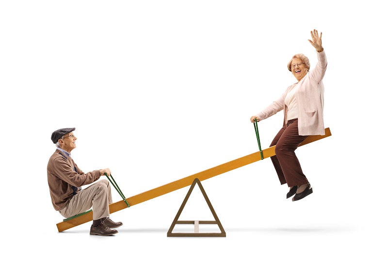 Full length profile shot of a senior man and woman waving and sitting on a seesaw isolated on white background